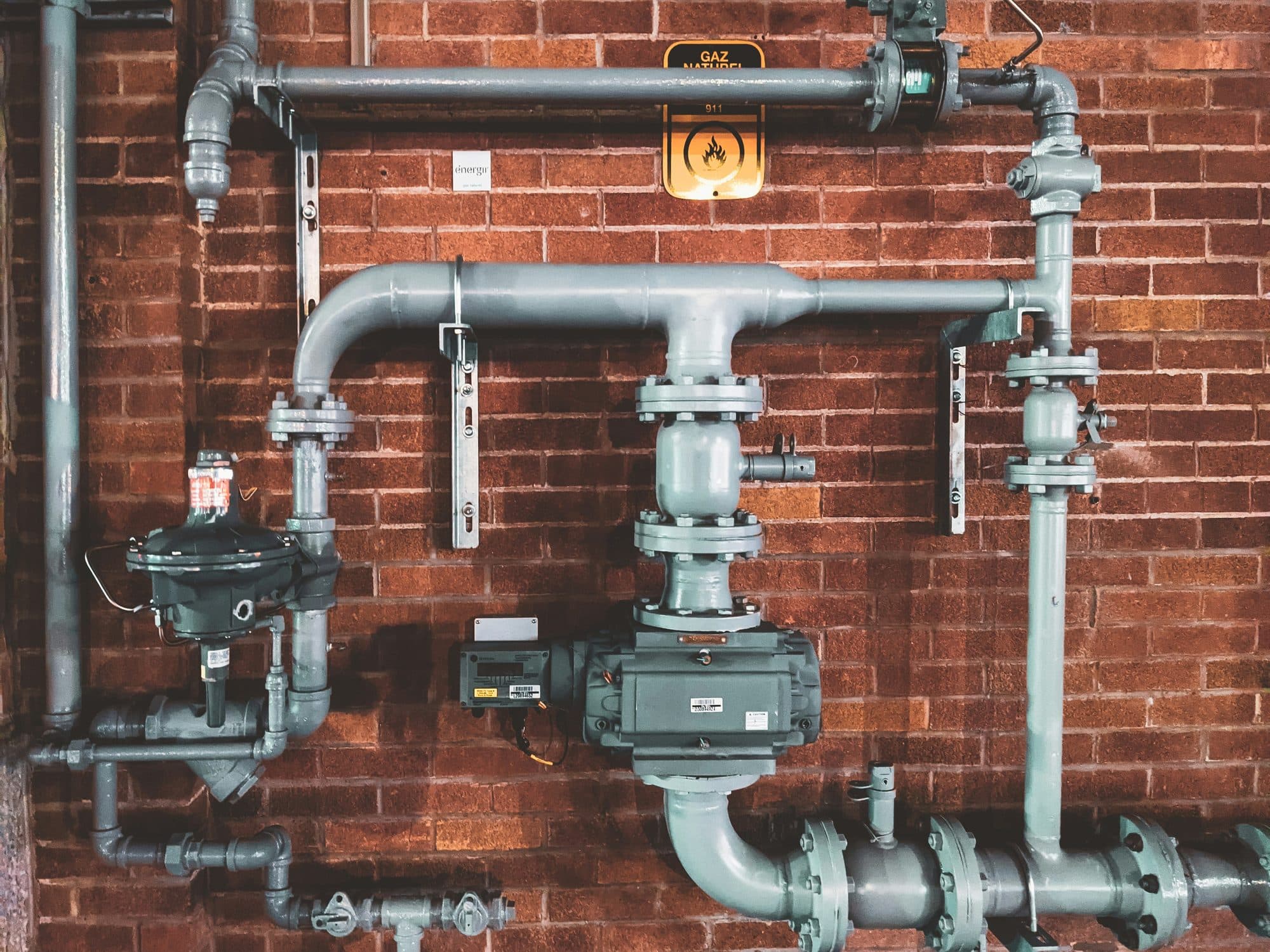 Iron pipes, valves and a water meter assembly mounted on a brick wall