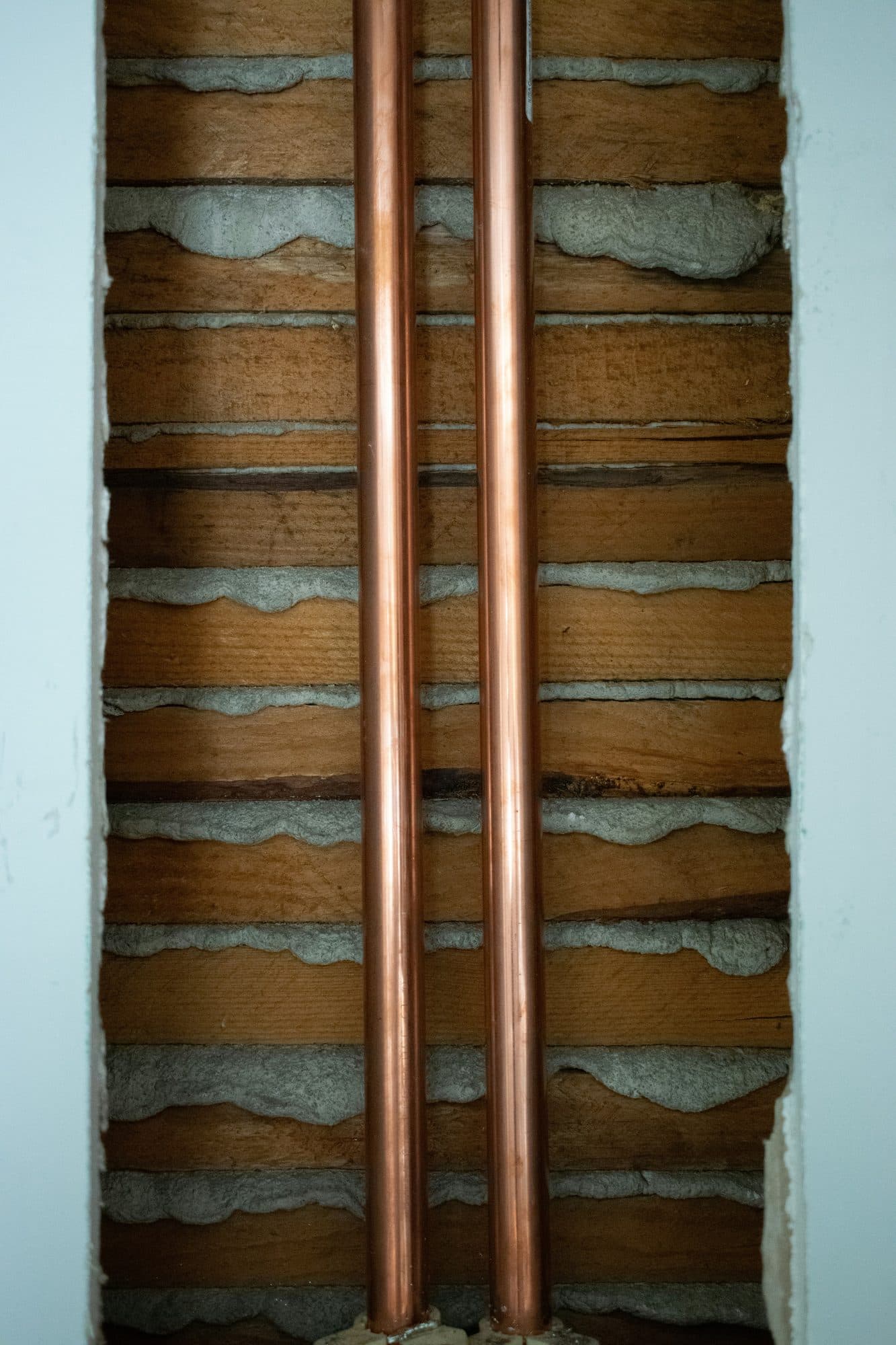 Two new copper supply lines run inside an opened lath-and-plaster wall