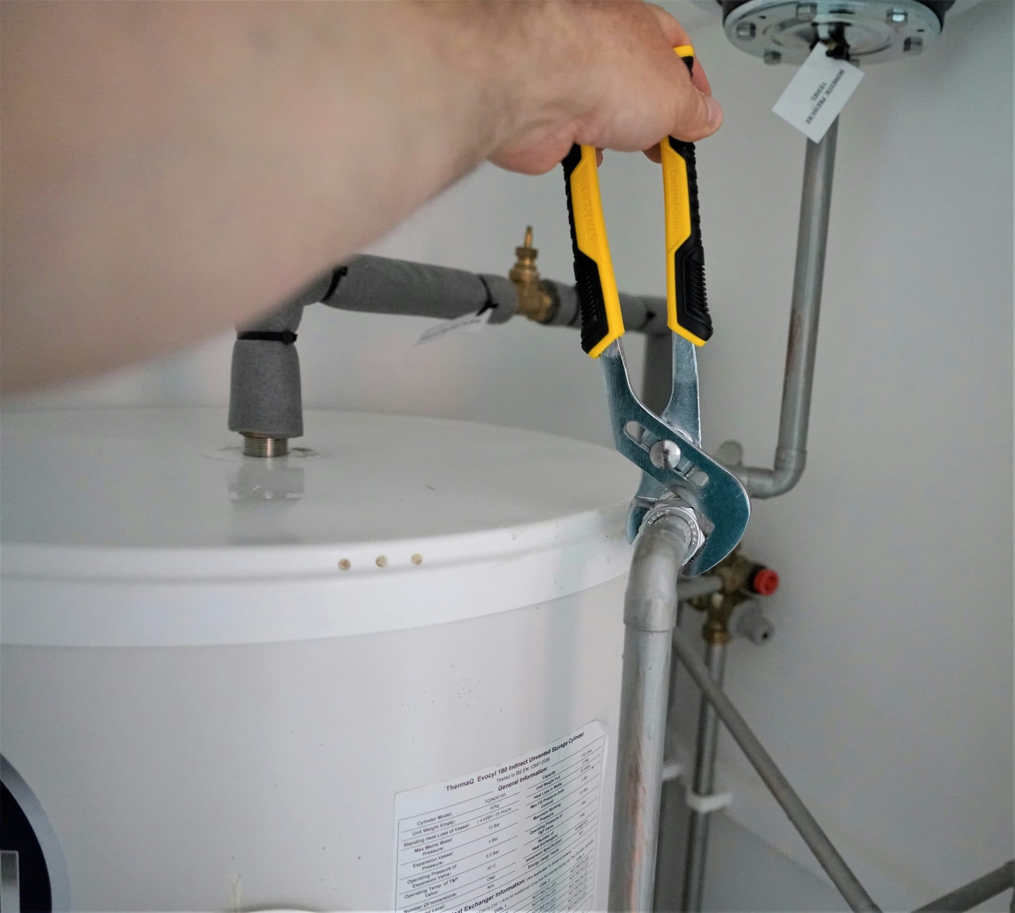 A plumber's hands tightening a fitting on top of a tank water heater